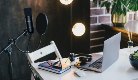 Items for recording podcast: professional microphone, earphones Items for recording podcast: professional microphone, earphones and laptop on white table in cozy home studio with black walls and lots of plants.